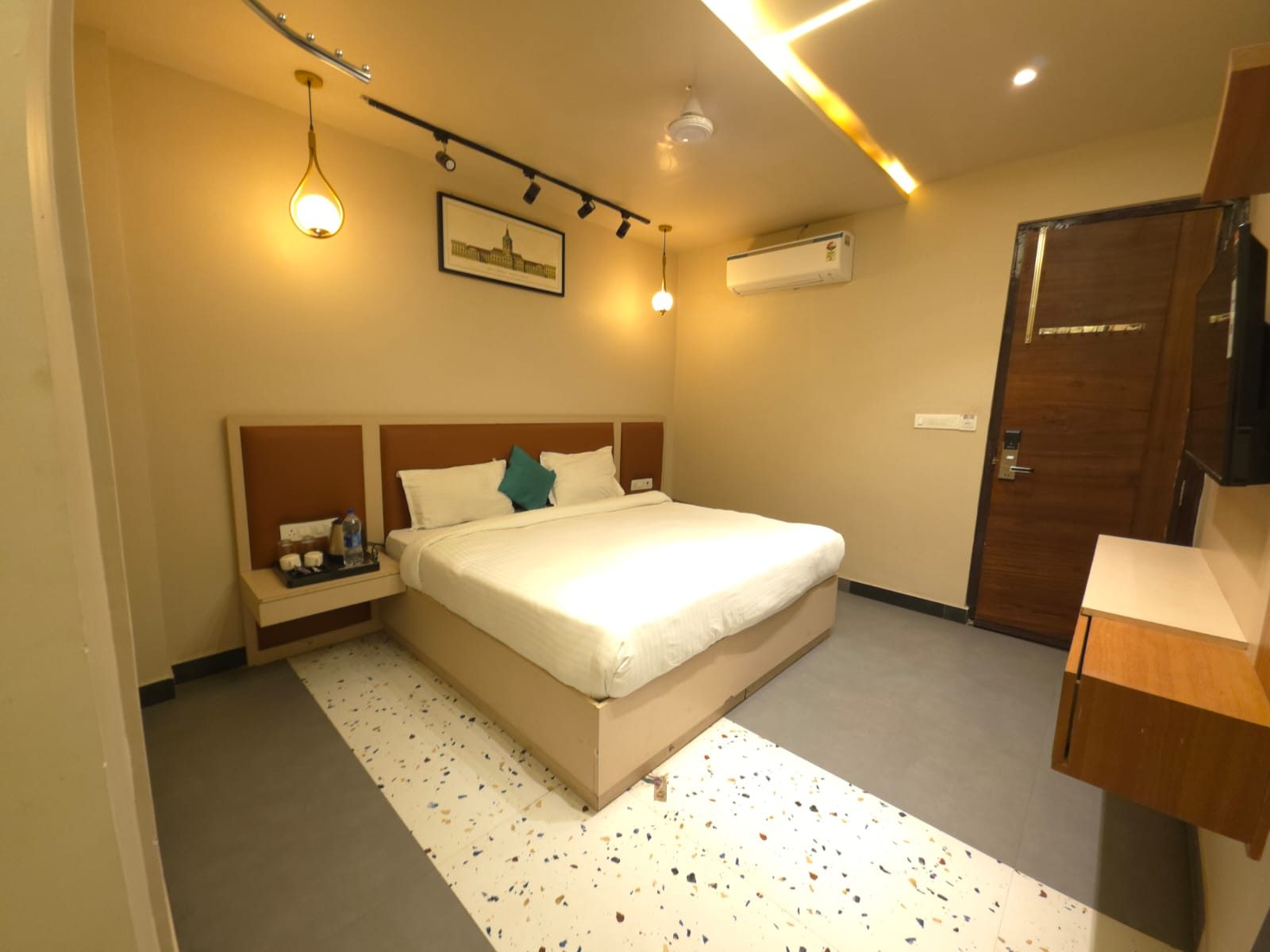 The Executive room in the evening: a king bed with white linen, track lights and a pendant lamp, a wall-mounted air conditioner and a dark wood door.